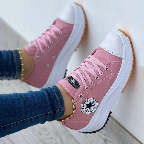 Pink canvas sneakers with white toe caps and soles, black logo, worn with blue jeans.