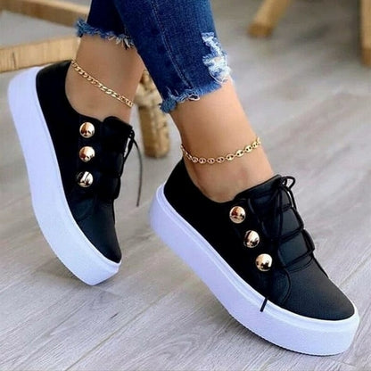 Black sneakers with white soles, gold buttons, worn with blue ripped jeans and ankle bracelets.