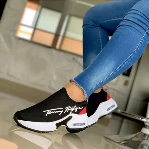 Close-up of a person wearing blue jeans and black sneakers with white soles and red accents.