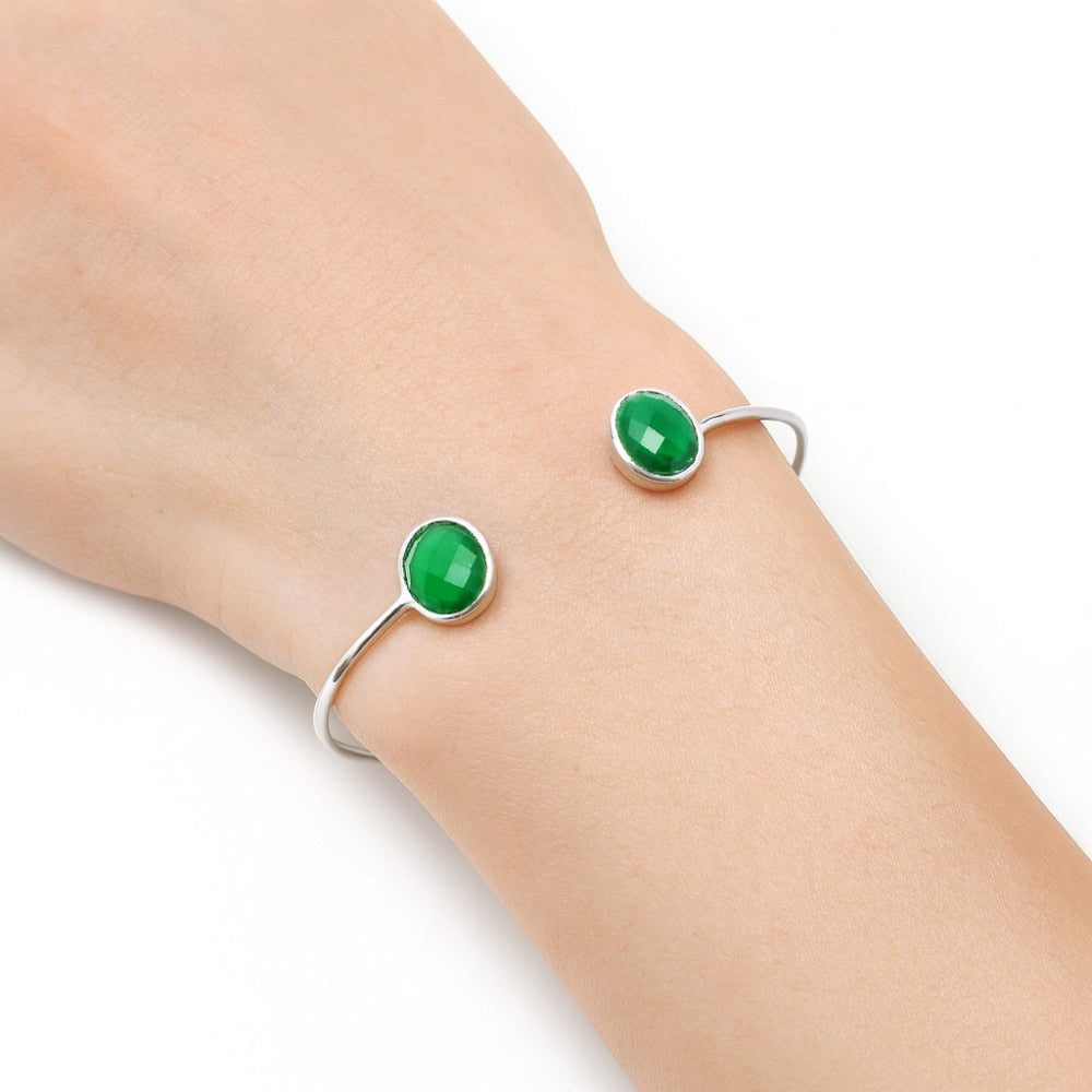 A silver bracelet with two oval green stones on a wrist against a white background.