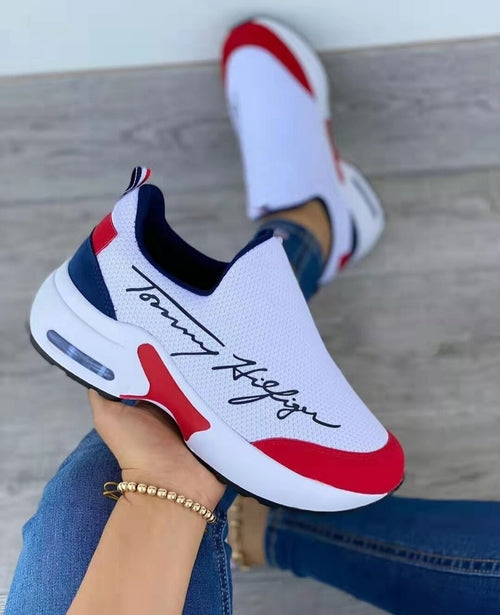 White sneakers with red and navy details, featuring a signature design and worn with blue jeans.