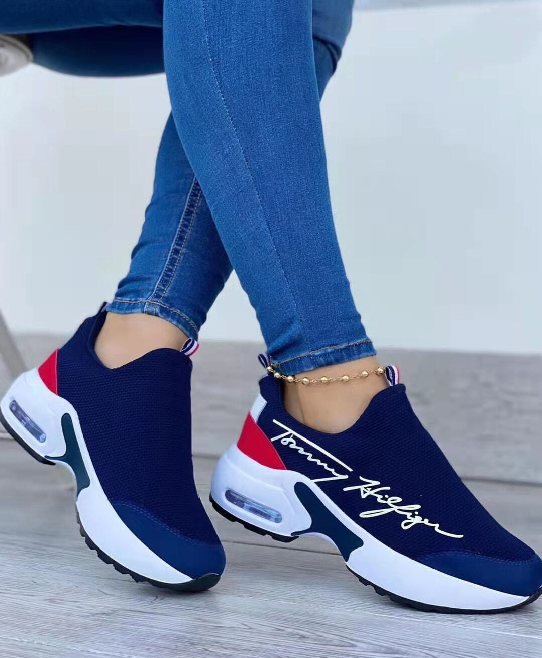 Blue sneakers with white soles and red accents worn with blue jeans on a wooden floor.