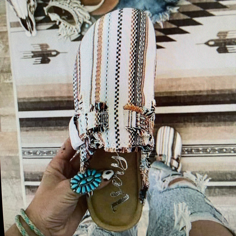 Colorful, striped slip-on shoe held in hand with turquoise ring, worn jean with frayed edges.