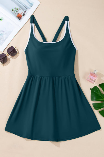 Teal dress with white trim, crisscross straps, sunglasses, book, perfume, and green leaves nearby.