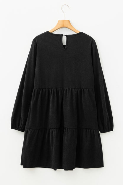 Black long-sleeve tiered dress on wooden hanger, featuring a buttoned keyhole back.