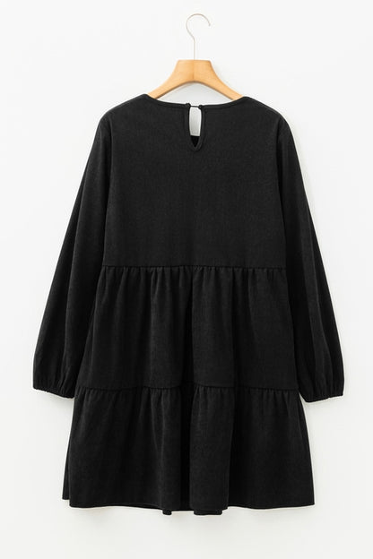 Black long-sleeve dress with tiered skirt on a wooden hanger against a white background.