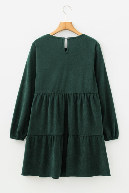 Dark green long-sleeve dress with tiered skirt and keyhole back, hung on a wooden hanger.