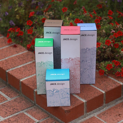 Colorful JACE.design boxes with city map patterns on brick steps, surrounded by red flowers.