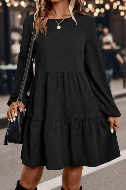 Woman wearing a black long-sleeve dress with layered skirt, holding a black purse.