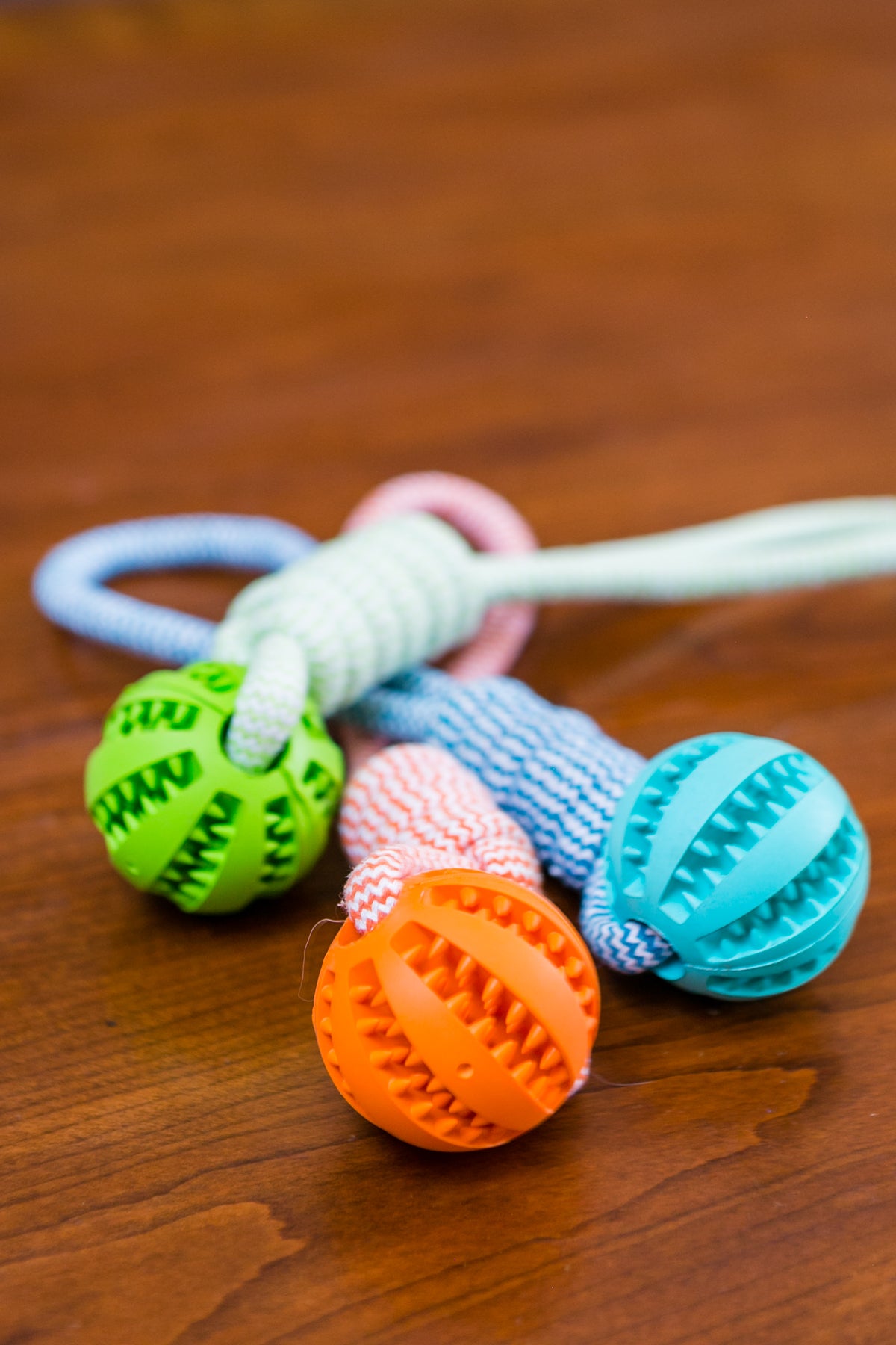Colorful dog toys with textured balls: green, orange, and blue on braided ropes, on wooden surface.