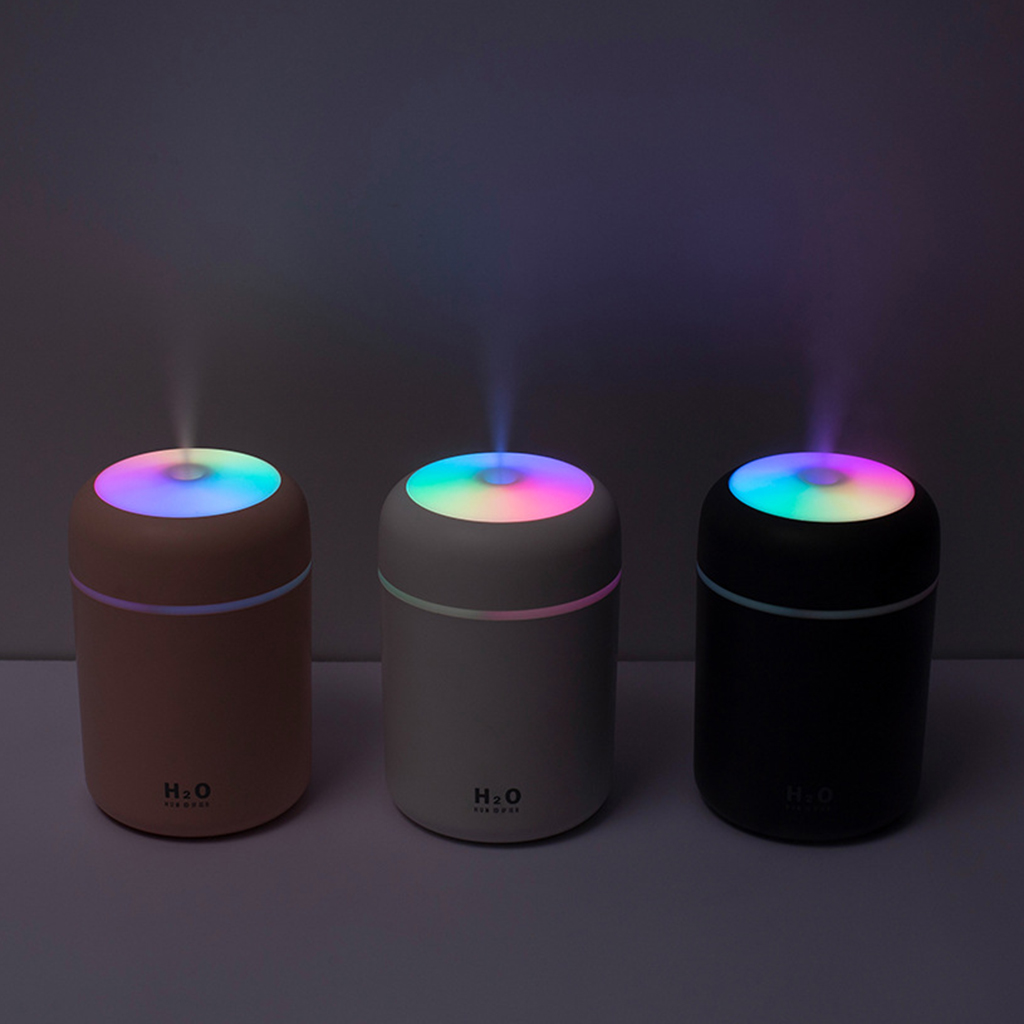 Three diffusers with colorful LED lights emitting mist in a dimly lit room.