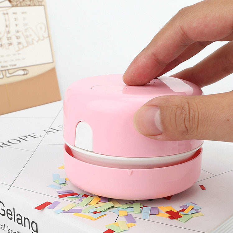 Hand pressing pink mini vacuum on confetti-covered surface.