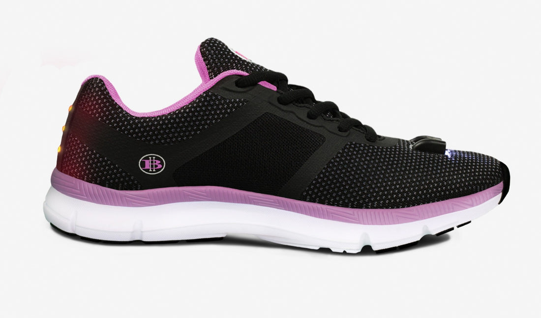 Black athletic shoe with a pink sole and trim, mesh texture, and white midsole on a white background.