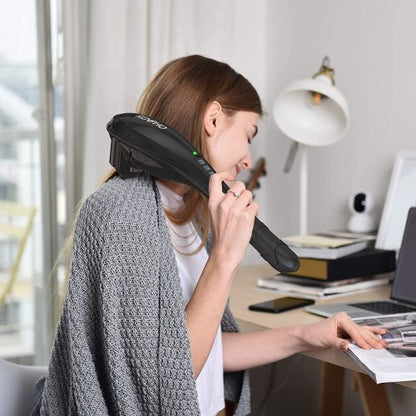 Woman using a black handheld massager on her neck in a home office with neutral colors.