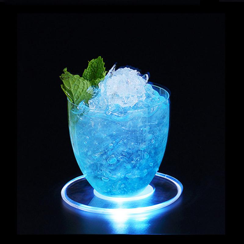 A glowing blue drink with ice and mint leaves on a lit coaster in a dark setting.