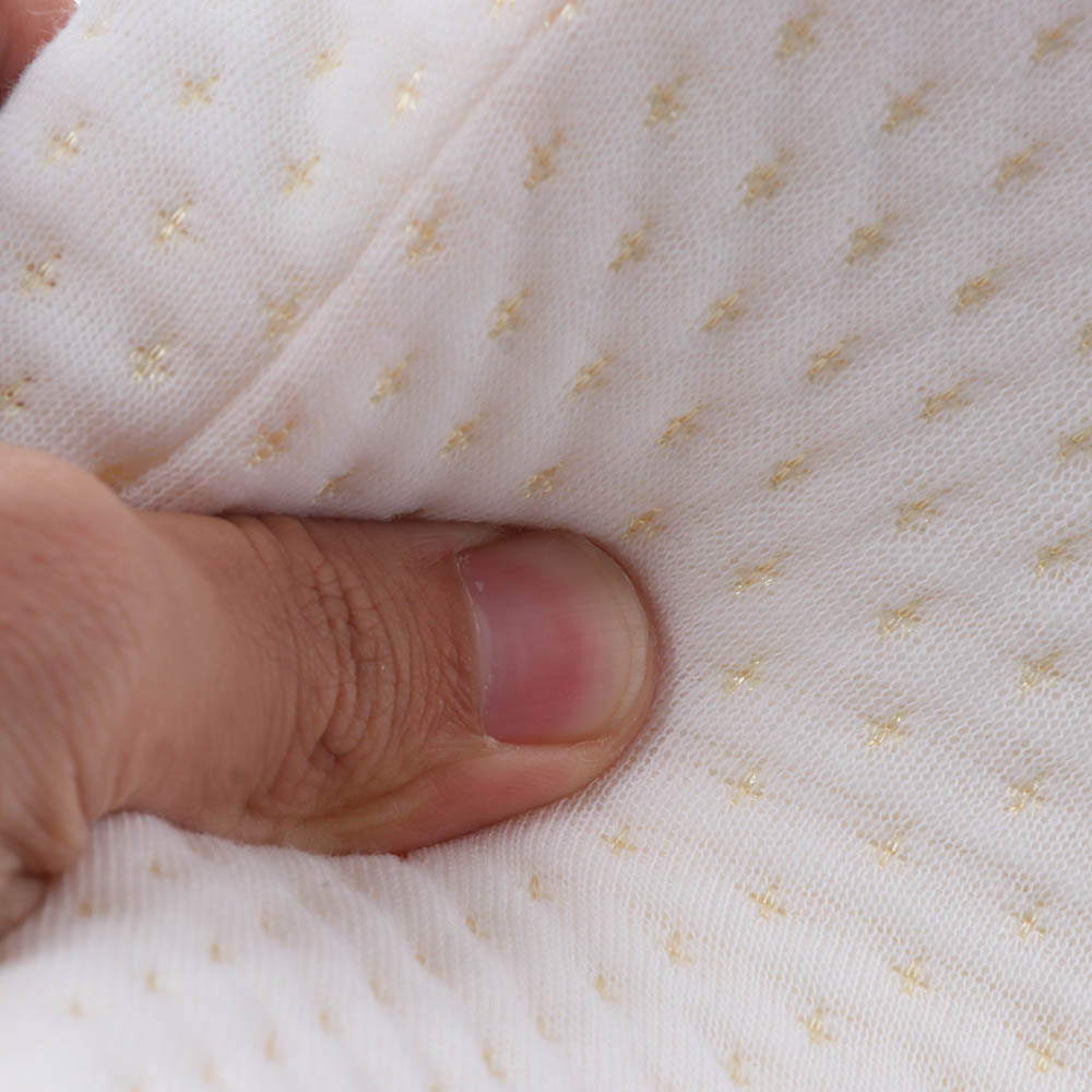 A hand pinches soft white fabric with small yellow dots creating a textured pattern.
