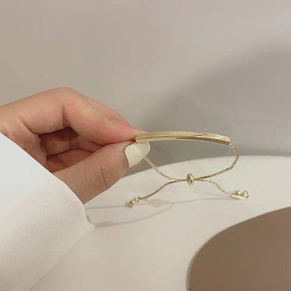 Hand holding a gold bracelet with a bar and adjustable chain on a light background.