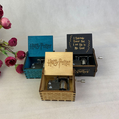 Three engraved wooden music boxes with "Harry Potter" themes, surrounded by pink flowers.