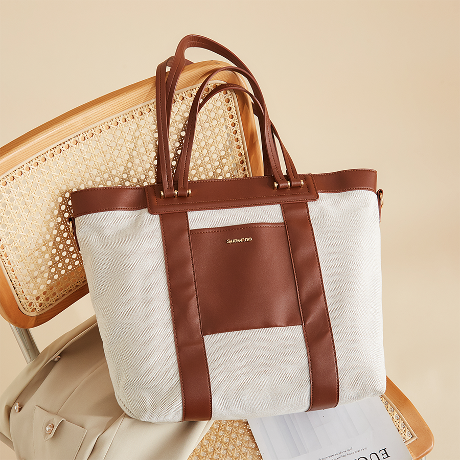 Brown and white tote bag on a woven chair, with a beige coat draped over the seat.