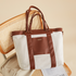 Brown and white tote bag on a woven chair, with a beige coat draped over the seat.
