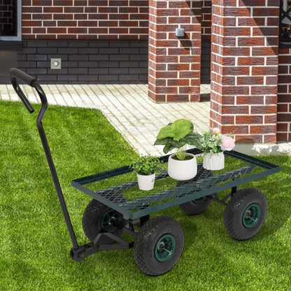 Green metal garden cart with four black wheels, holding potted plants, on lush grass near brick wall.