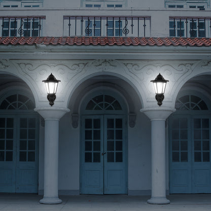 Illuminated porch with two black lanterns on white pillars, arched doors, and wrought iron balcony.