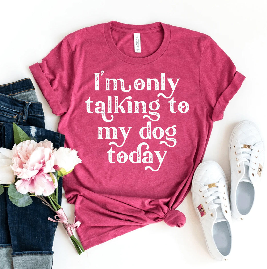 Pink T-shirt with white text, jeans, flowers, and white sneakers on a white background.