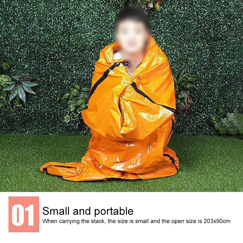 Person wrapped in an orange emergency blanket, against a green leafy background, sitting on grass.