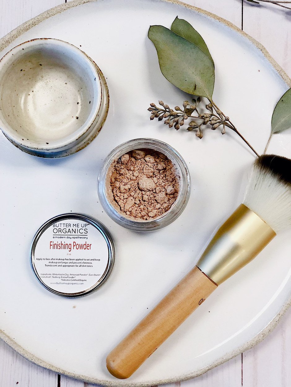 Makeup powder, brush, and leaf on a white plate; earthy tones and minimal aesthetic.