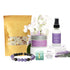 A spa gift set with lavender bottle, candle, bracelet, floral bath salts, and white flowers.