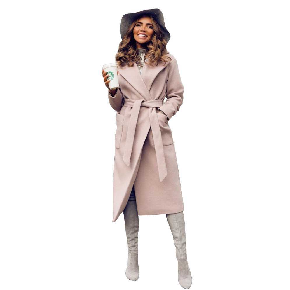 Woman in a beige coat and hat, holding a coffee cup, smiling, wears knee-high boots.