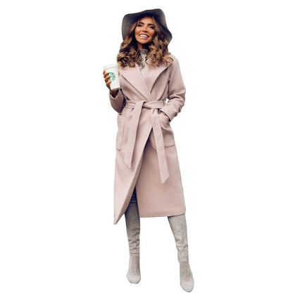 Woman in a beige coat and hat, holding a coffee cup, smiling, wears knee-high boots.