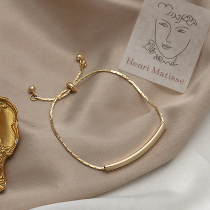 Gold bracelet on beige fabric with gold accents and a Matisse sketch card beside it.