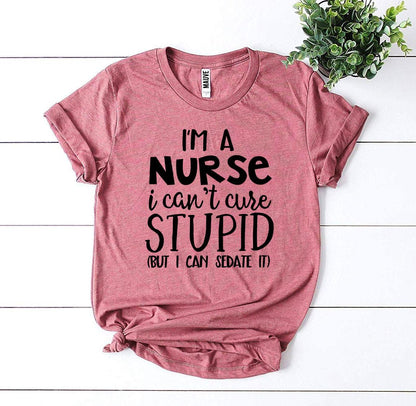 Pink t-shirt with humorous black text on a white backdrop, beside a small green plant.