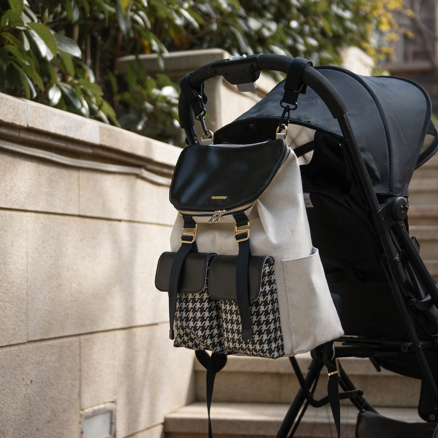 Stroller with a stylish beige and black houndstooth backpack hanging on the handle.