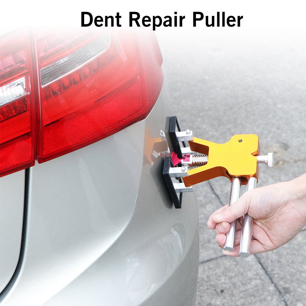 Gold dent puller on silver car bumper near red tail light, hand holding tool.
