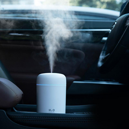 White portable humidifier emitting mist, placed in a car cup holder beside dark seats.