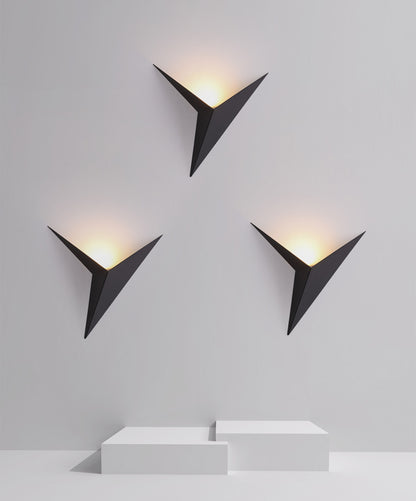 Three black triangular wall lights on a white wall with soft yellow glow, above white geometric blocks.