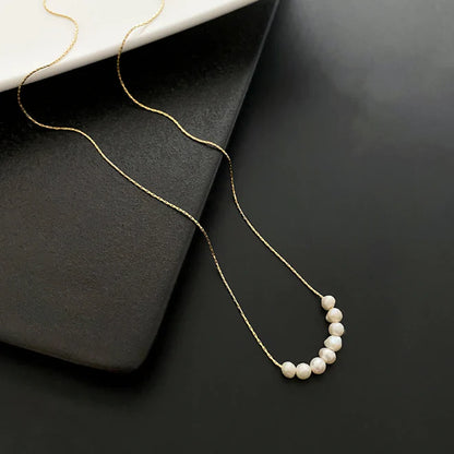 Gold chain with small white pearls on black and white surfaces.