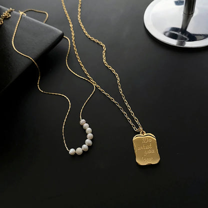 Two gold necklaces on black surface; one with pearls, one with engraved pendant "Do what you love."