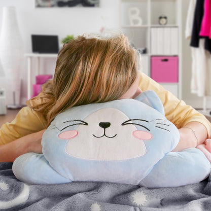 Person hugging a smiling blue cat pillow with pink cheeks, in a cozy room with soft colors.