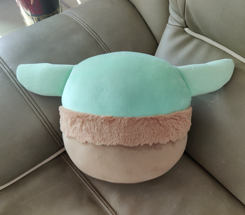 Plush pillow with green ears, light brown face, and fluffy tan band, on a gray couch.