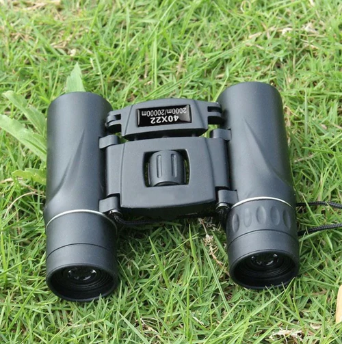 Black binoculars on green grass, featuring a central focus wheel and engraved specifications.