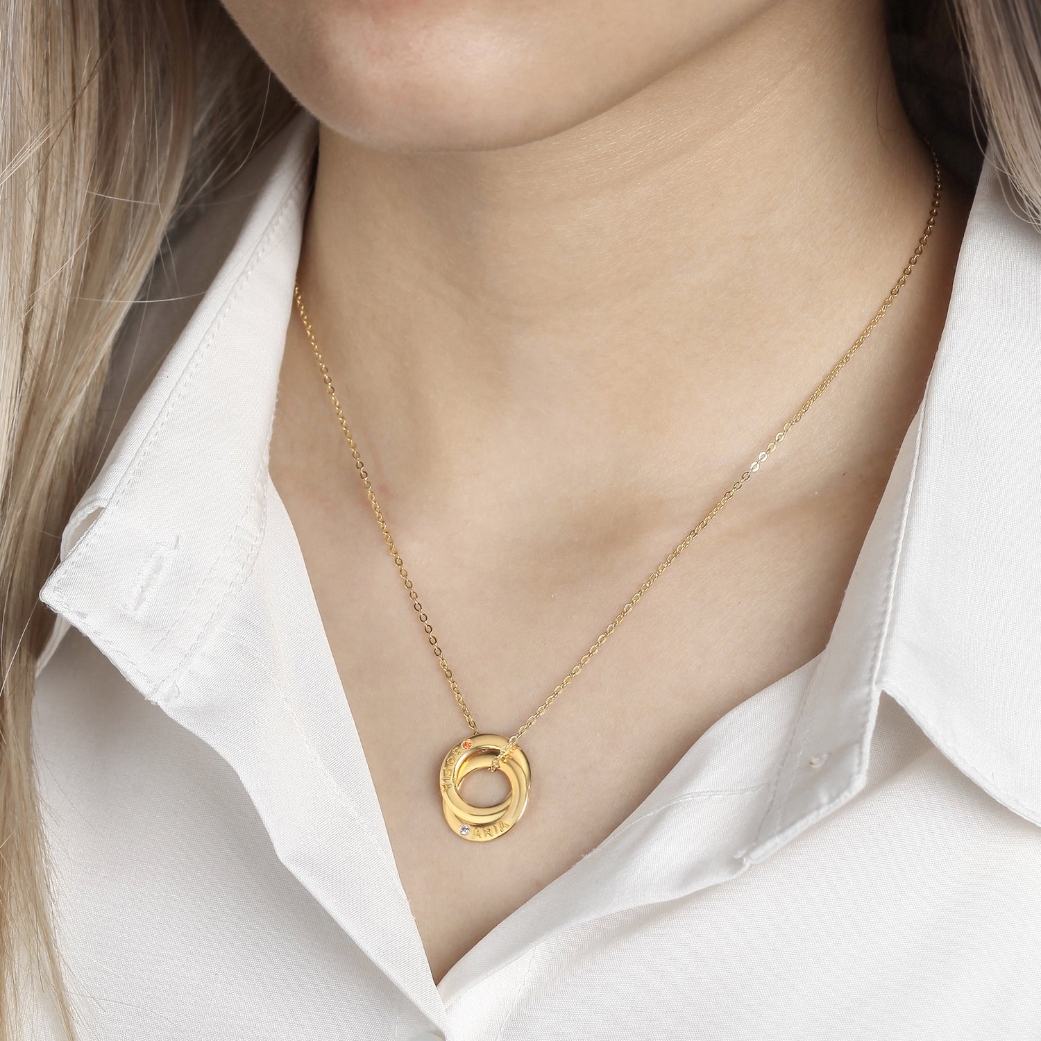 A gold necklace with interlocking rings on a woman wearing a white shirt.