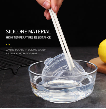 Hand holding chopsticks with silicone mold in clear bowl of water, lemon in background.