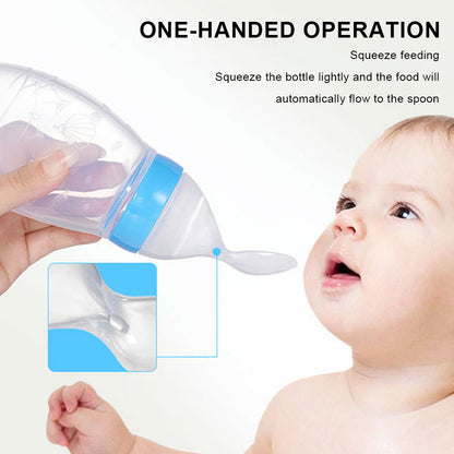 Hand squeezing a transparent bottle with a blue cap, feeding a baby with an attached spoon.