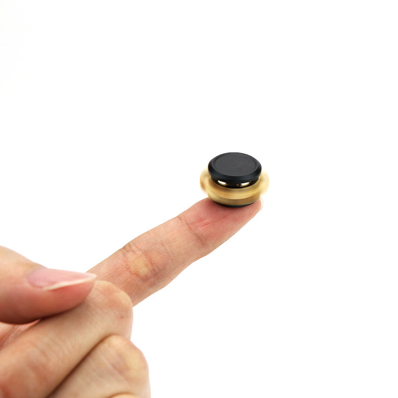 Finger balancing a small black and gold magnetic spinner against a white background.