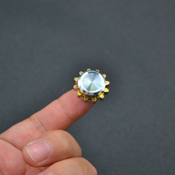 A small, metallic gear with a reflective, silver center is balanced on a fingertip.