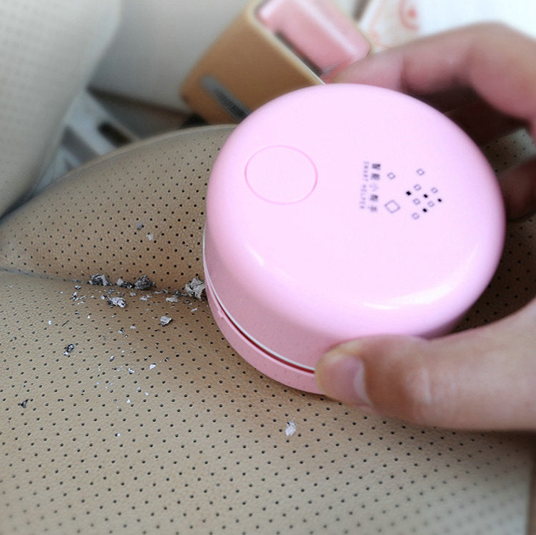 Pink handheld vacuum cleaning crumbs on a beige perforated car seat.