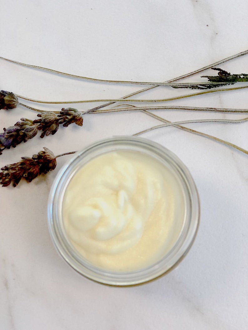 A jar of creamy substance on white marble with dried lavender sprigs beside it.